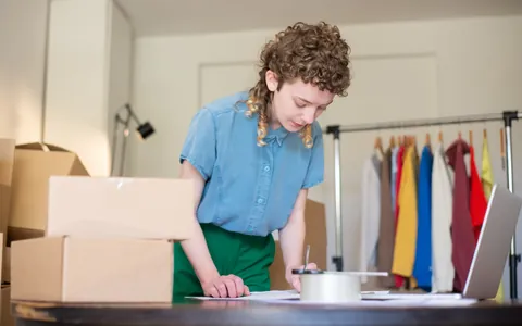 Online seller packing orders next to a clothing rack